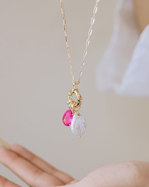 Gold chain pendant with gemstones and a pearl on an open hand
