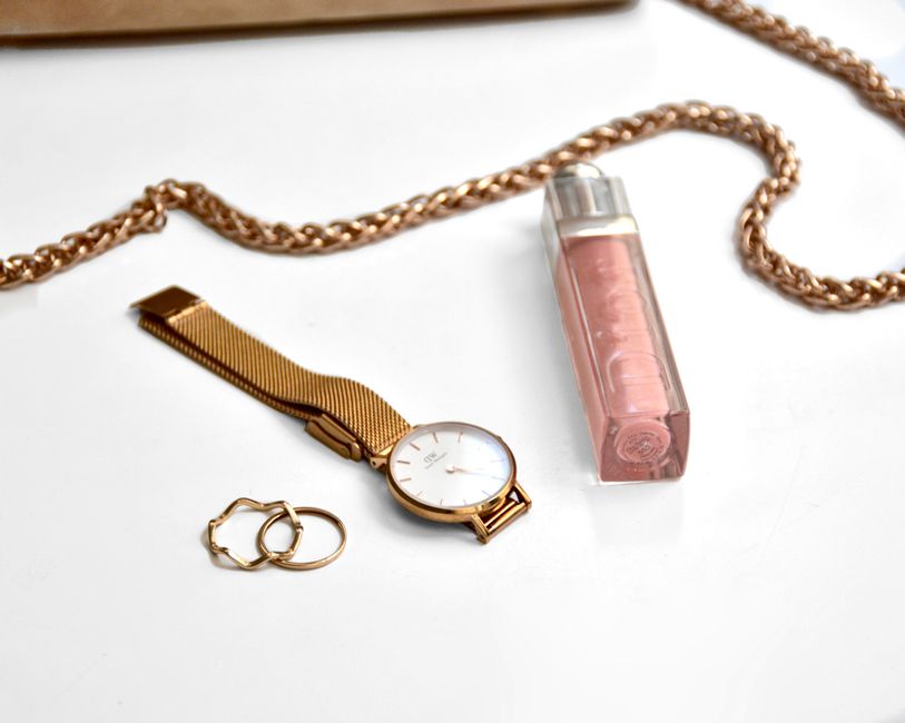 Flat lay of gold wristwatch, rings, and chain on a white surface
