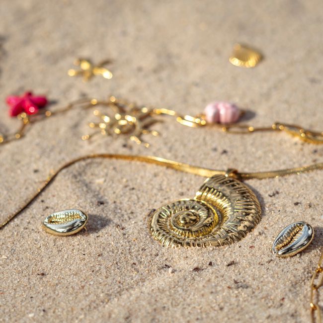 Gold jewelry with seashell designs scattered on beach sand