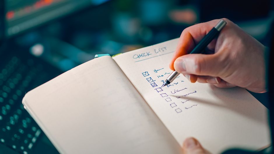 Close-up of a hand writing in a notebook with a checklist