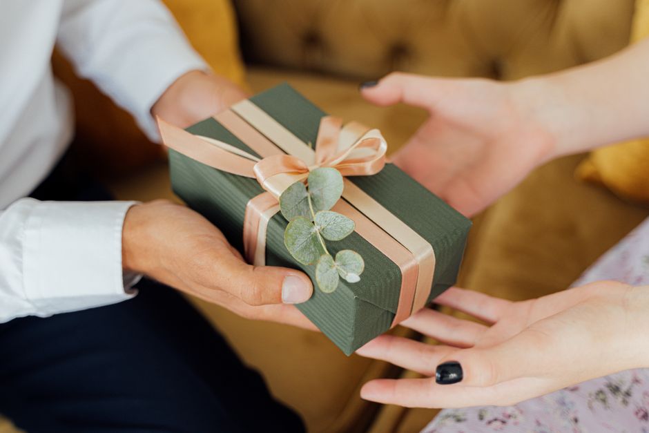 Two hands exchanging an elegantly wrapped gift box with ribbons