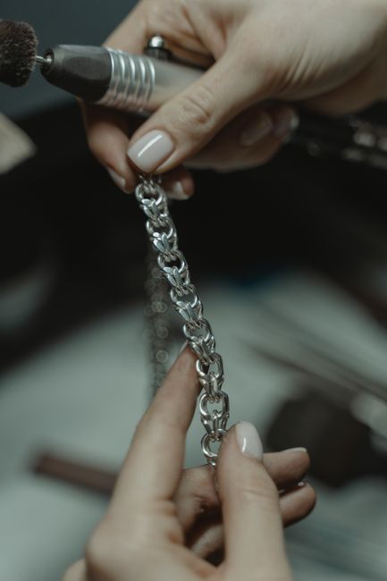 Close-up of a jeweler polishing a silver chain with a tool