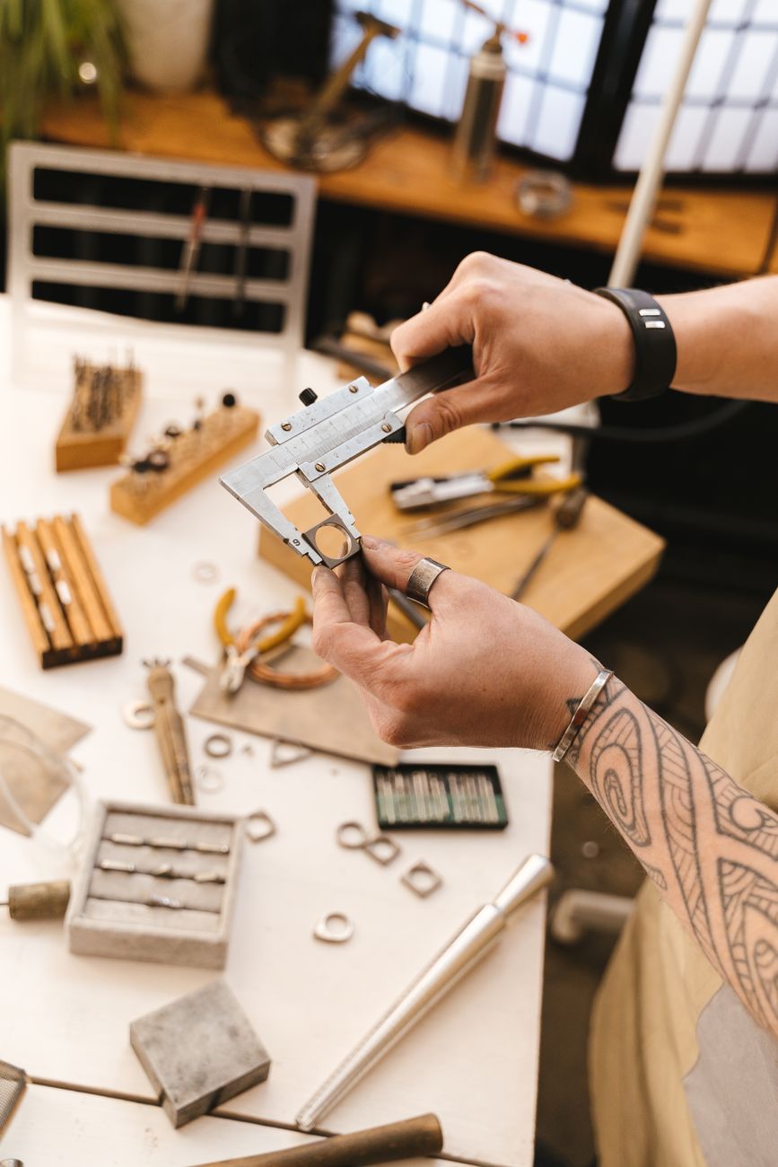 Hands measuring jewelry gauge with a caliper in a workshop