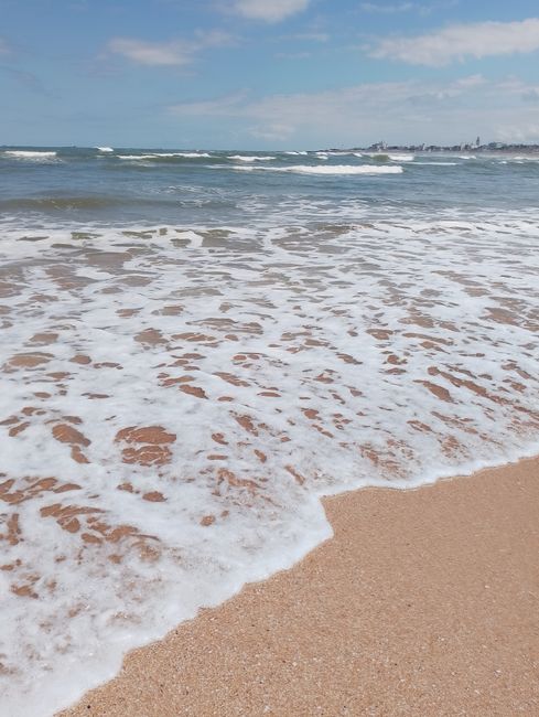 Gentle ocean waves wash over a sandy beach under a clear sky