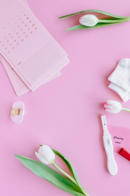 Pink flat lay of baby essentials, tulips, and a positive pregnancy test