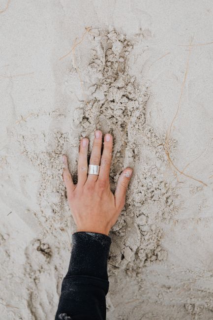Overhead view of a hand with a silver ring pressing into sand