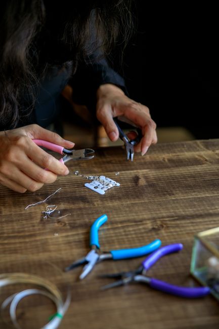 Person making jewelry with pliers and beads on a wooden table